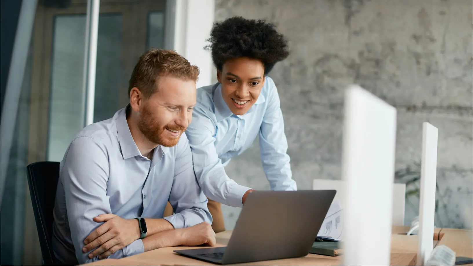 2 people smiling whilst reading a report on a laptop